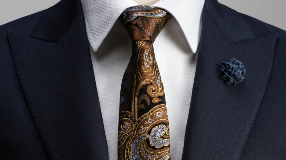 Cravate en soi marron à motif paisley portée avec une chemise blanche et u costume bleu marine