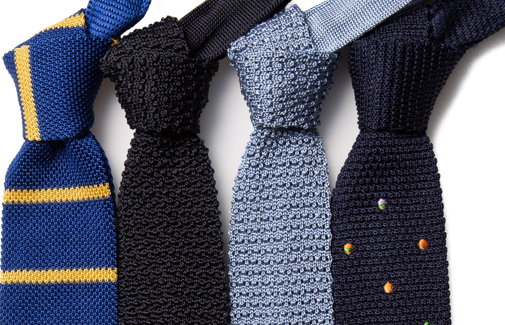 Quatre style de cravates tricot différents : une rayée, une unie bleu marine, une unie bleu clair et une bleu marine à pois