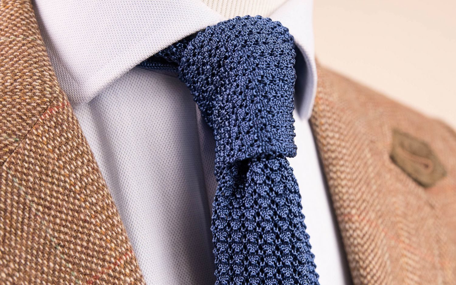 Blue knit tie worn by a wooden dummy with a white shirt and beige tweed jacket